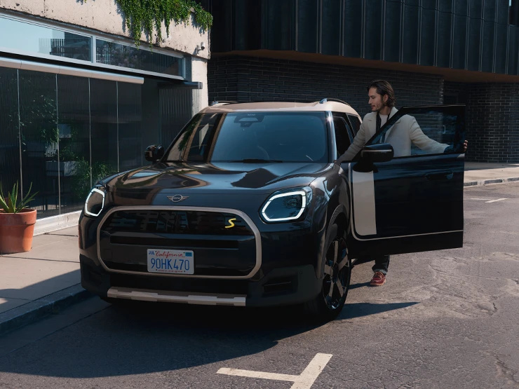 Frontansicht eines vollelektrischen MINI Countryman in Midnight Black mit Dach in Vibrant Silver auf einer Straße.