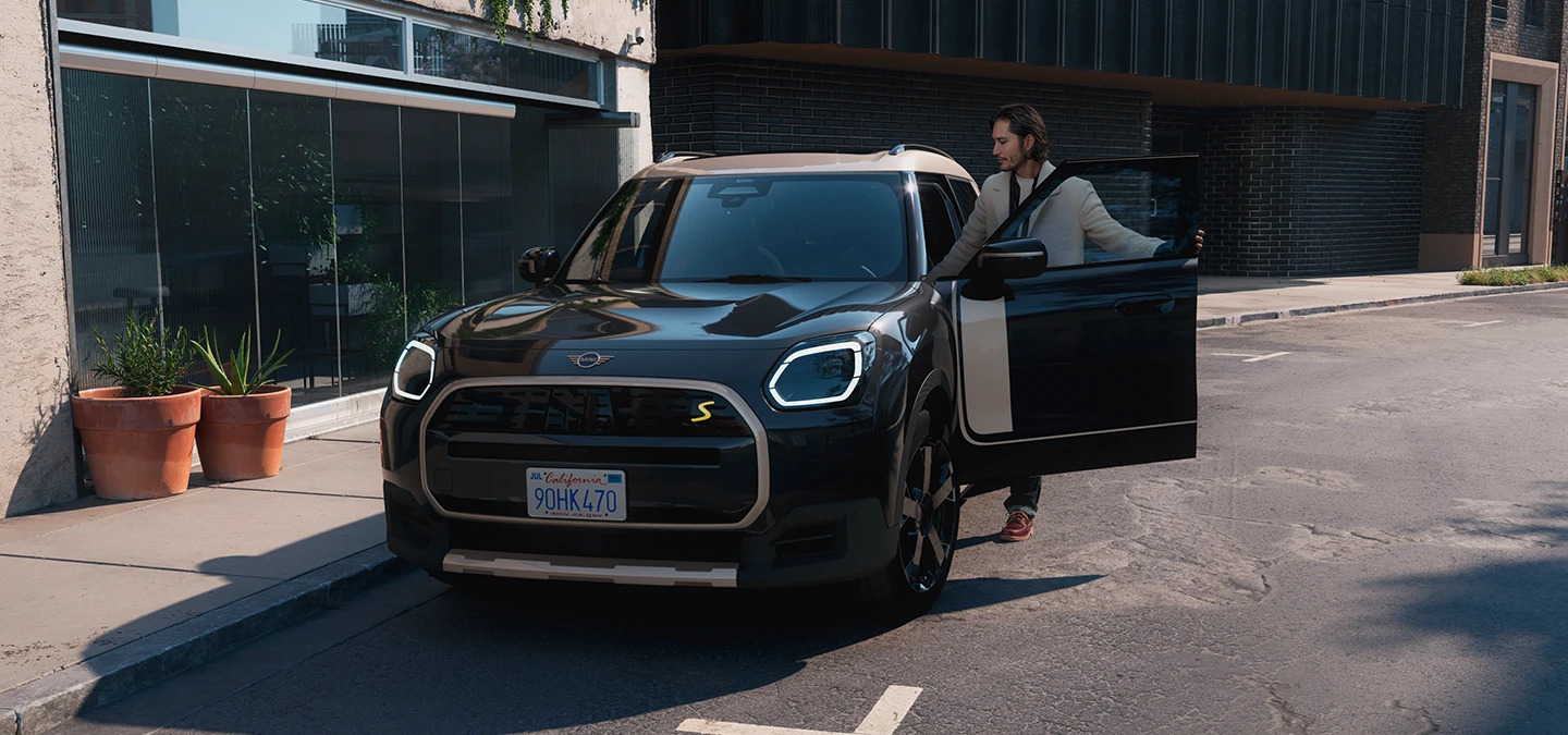 Frontansicht eines vollelektrischen MINI Countryman in Midnight Black mit Dach in Vibrant Silver auf einer Straße.