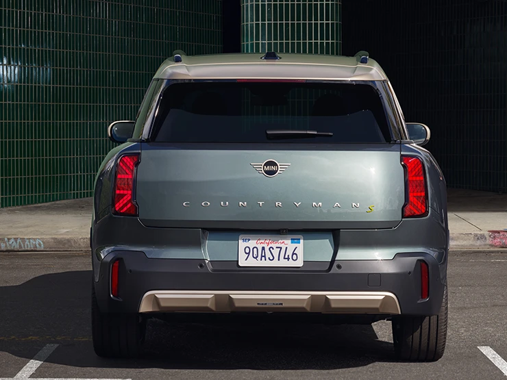 Heckansicht eines parkenden vollelektrischen MINI Countryman in Smokey Green mit Dach in Vibrant Silver. 