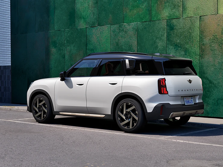 Seitliche Heckansicht des MINI Countryman in Nanuq White mit schwarzem Dach, der auf einer Straße steht.