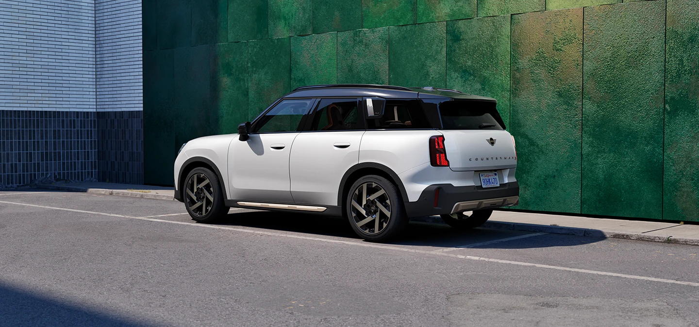 Seitliche Heckansicht des MINI Countryman in Nanuq White mit schwarzem Dach, der auf einer Straße steht.