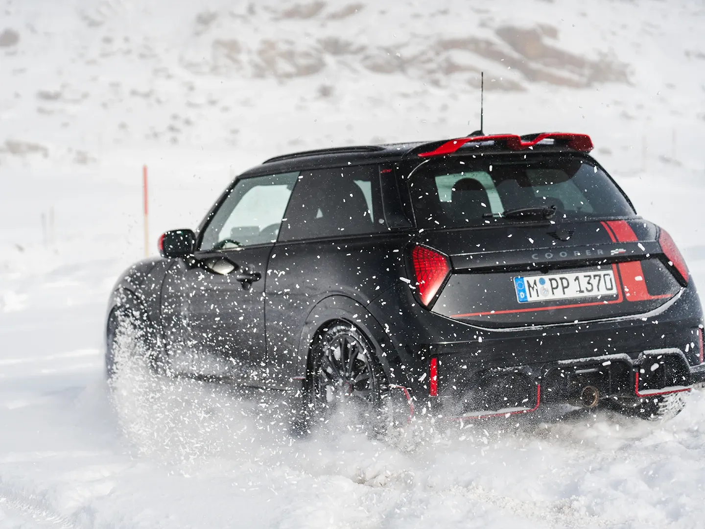 Ansicht von hinten auf einen MINI Cooper JCW, der durch den Schnee fährt.