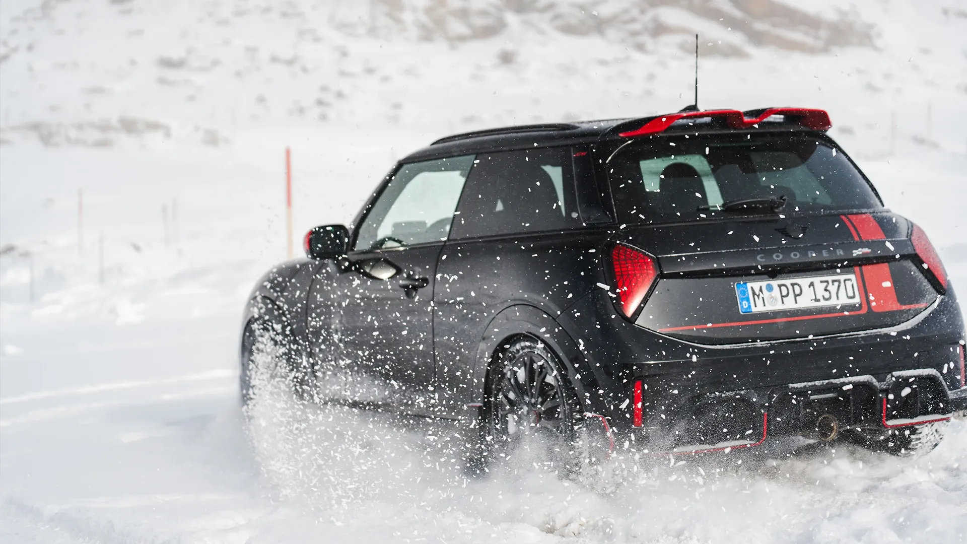 Ansicht von hinten auf einen MINI Cooper JCW, der durch den Schnee fährt.