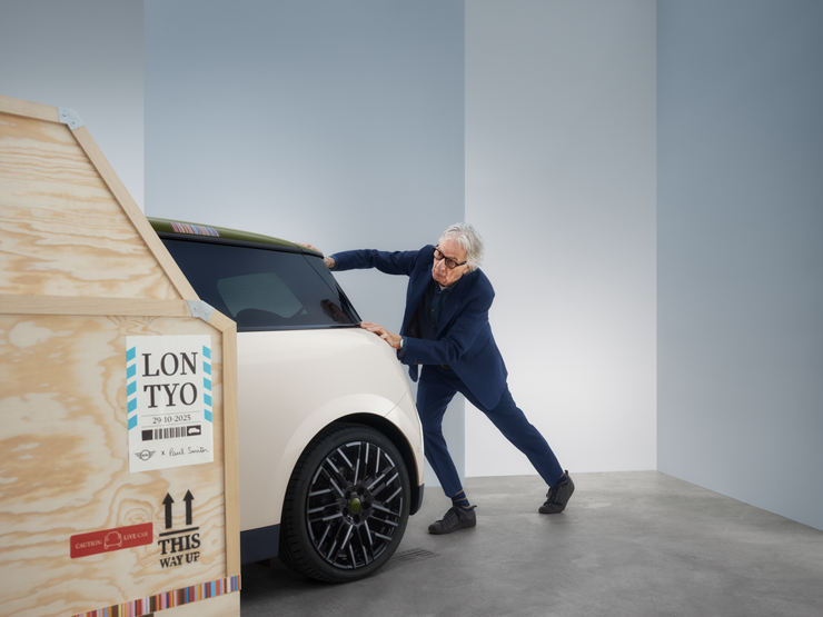 Heckansicht des vollelektrischen MINI Cooper Paul Smith Edition in Inspired White mit Paul Smith hinter dem Auto.