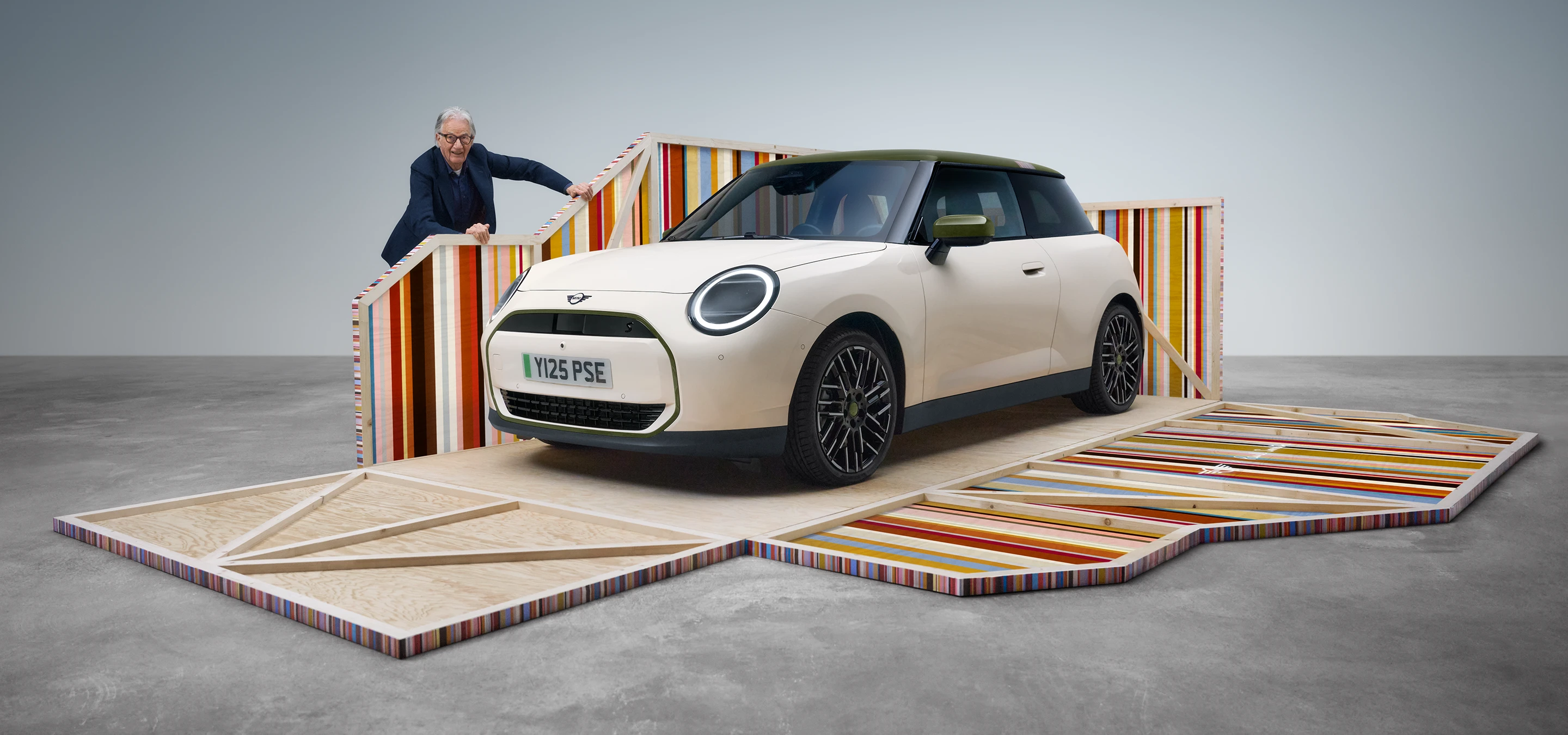 Frontansicht des vollelektrischen MINI Cooper Paul Smith Edition in Inspired White mit dem Designer Paul Smith.